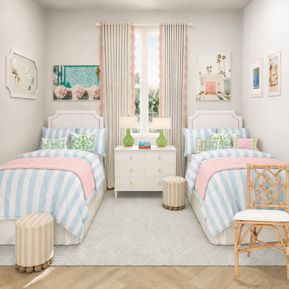 A bright, symmetrical children's bedroom featuring two single beds with light blue and white striped bedding and pink throws, a white nightstand with green lamps, striped stools, and a rattan chair on a light rug.